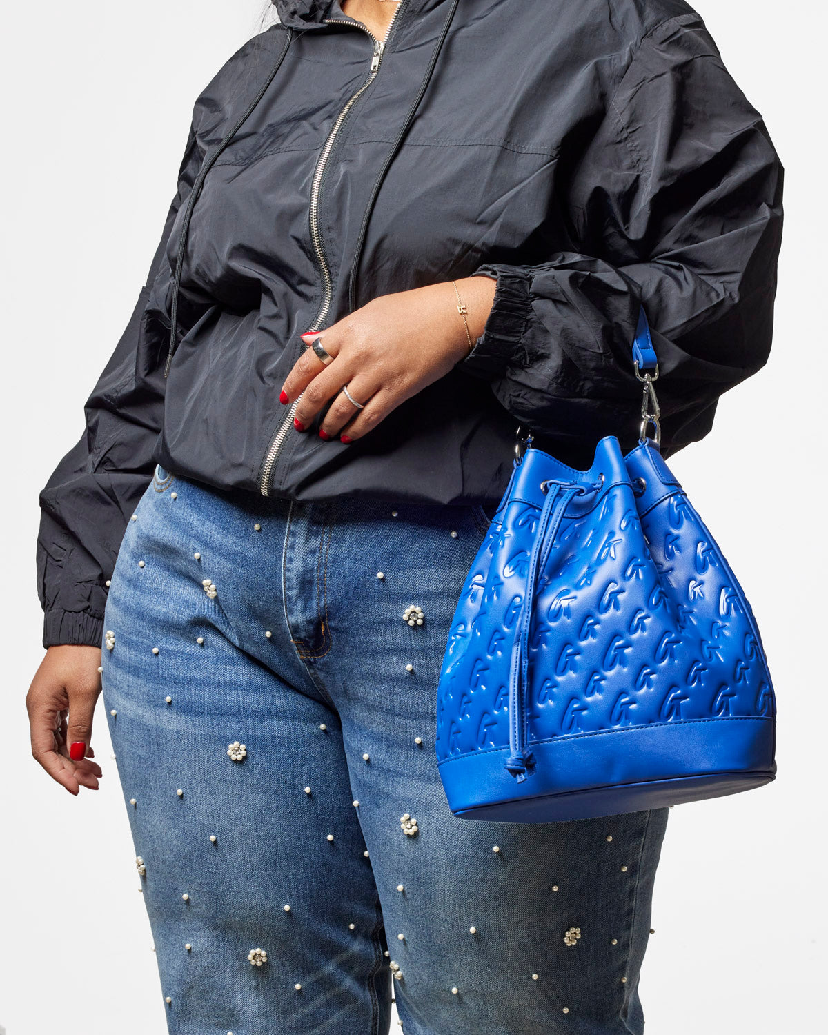 Large blue monogram bucket bag held by a person wearing a black jacket and embellished jeans, showcasing stylish design.