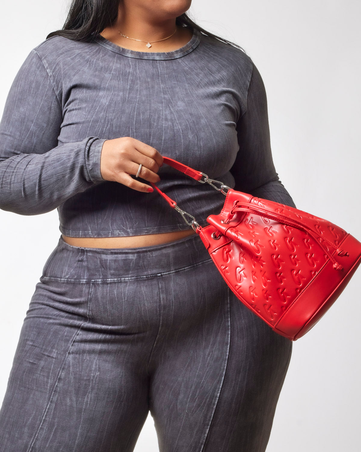 Model holding a red medium monogram bucket bag, styled with a matching gray outfit for a chic look.
