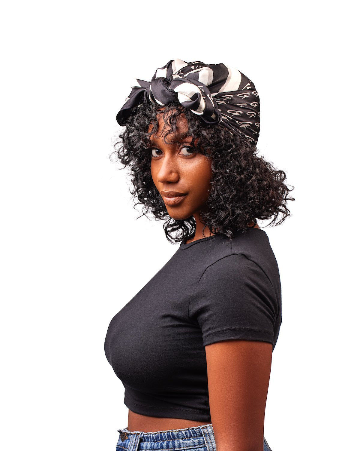 Woman wearing a large black silk scarf with monogram pattern, styled as a headwrap, against a white background.