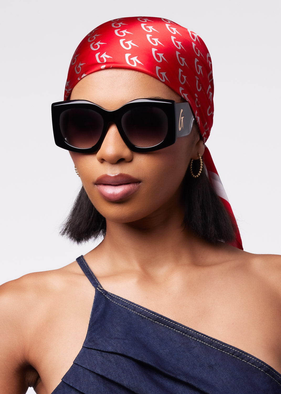 Model wearing a large red monogram silk scarf tied around her head, paired with oversized black sunglasses and a stylish top.