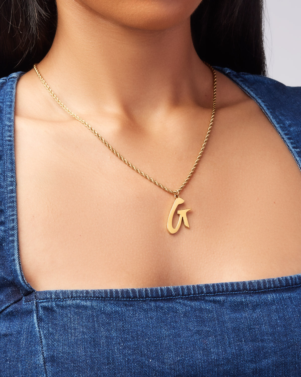 Gold GAL necklace featuring a stylish pendant on a twisted chain, elegantly worn against a denim top.