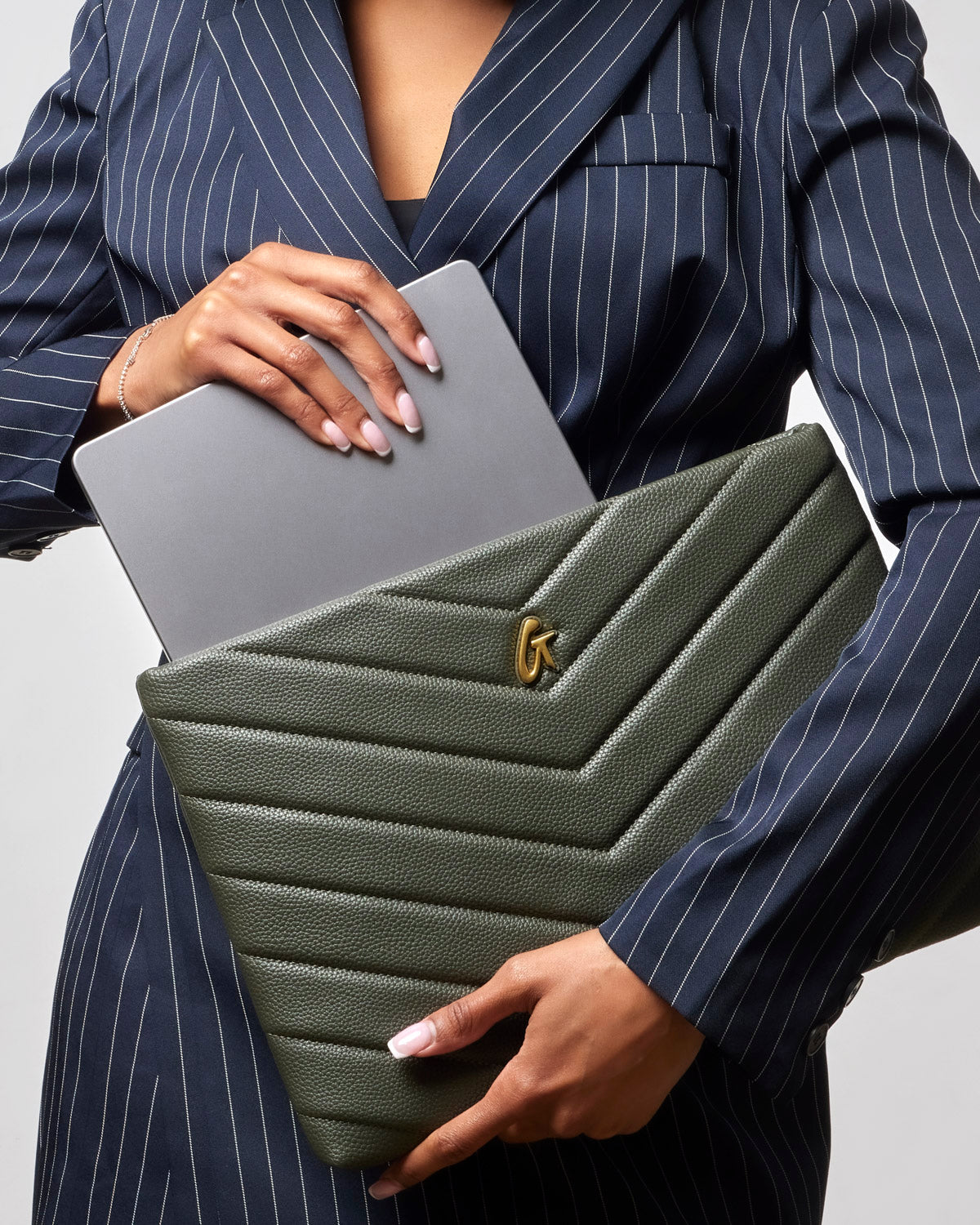Olive green pebble laptop sleeve with chevron design, held by a woman in a pinstripe suit, showcasing a laptop.