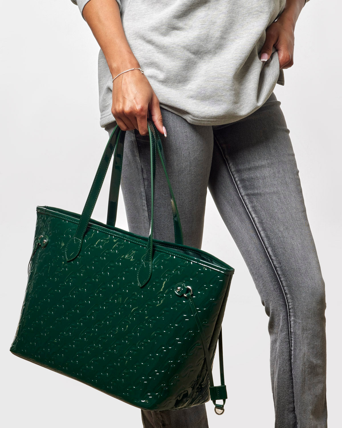 Mirror green monogram glam tote with wristlet, held by a woman in casual attire, showcasing its stylish design.