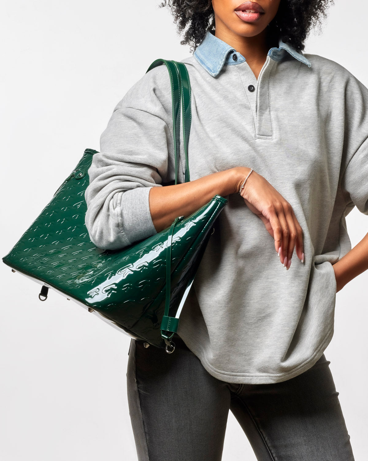 Mirror green monogram glam tote with wristlet, stylishly held by a woman in a gray sweatshirt and jeans.