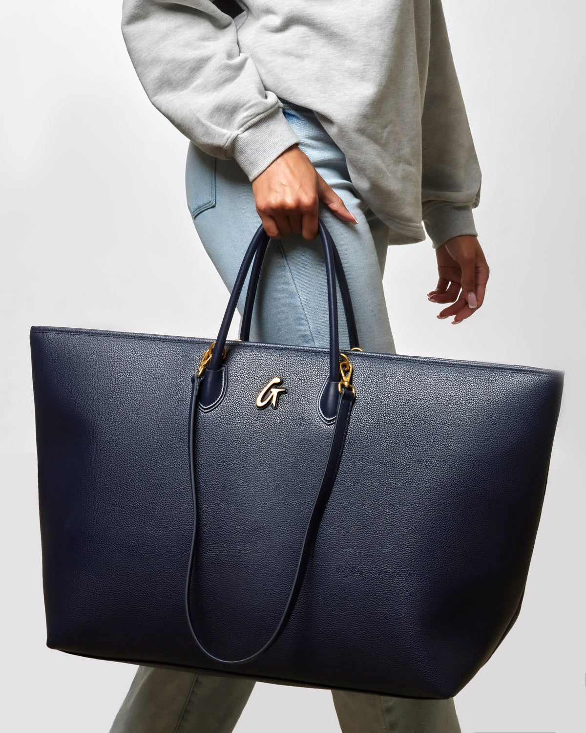 Navy jumbo pebble tote bag with gold accents, carried by a woman in a casual outfit, perfect for stylish everyday use.
