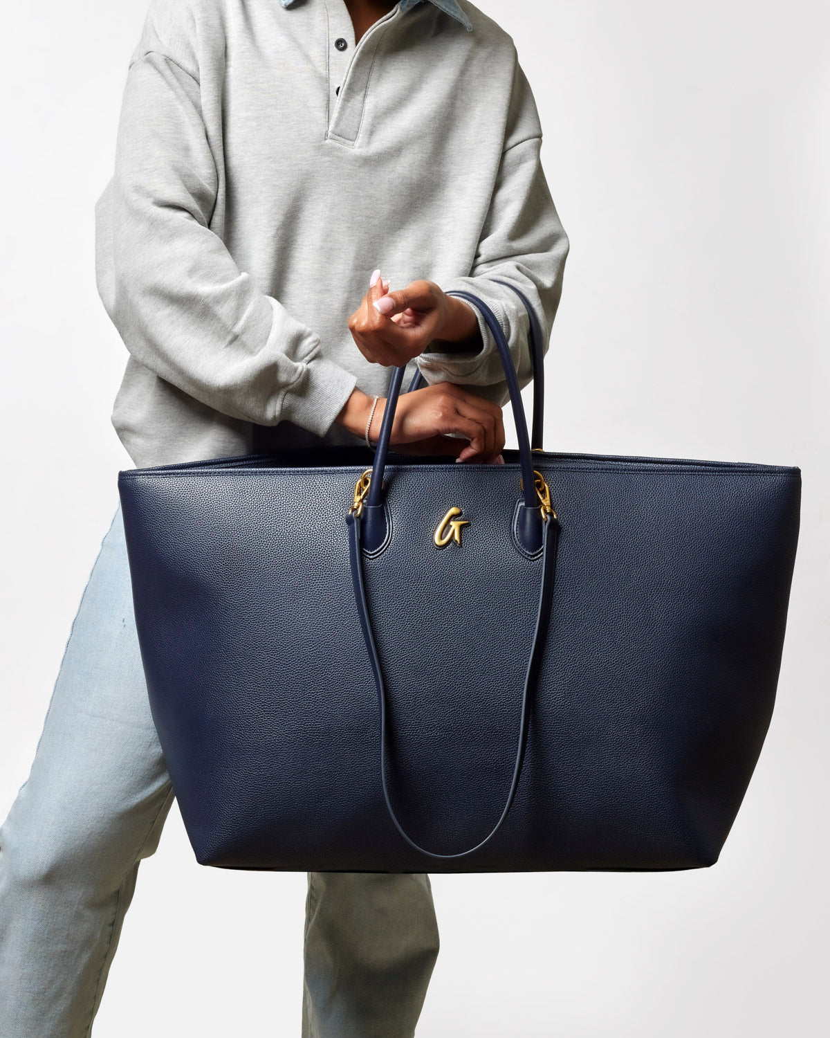 Navy jumbo pebble tote bag with gold accents, held by a person in a casual outfit, showcasing its spacious design.