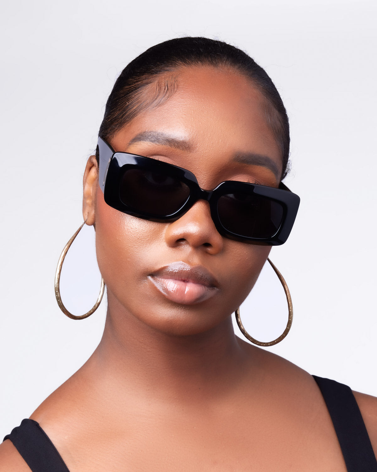Chic woman wearing oversized black sunglasses and gold hoop earrings, showcasing a stylish, modern look.