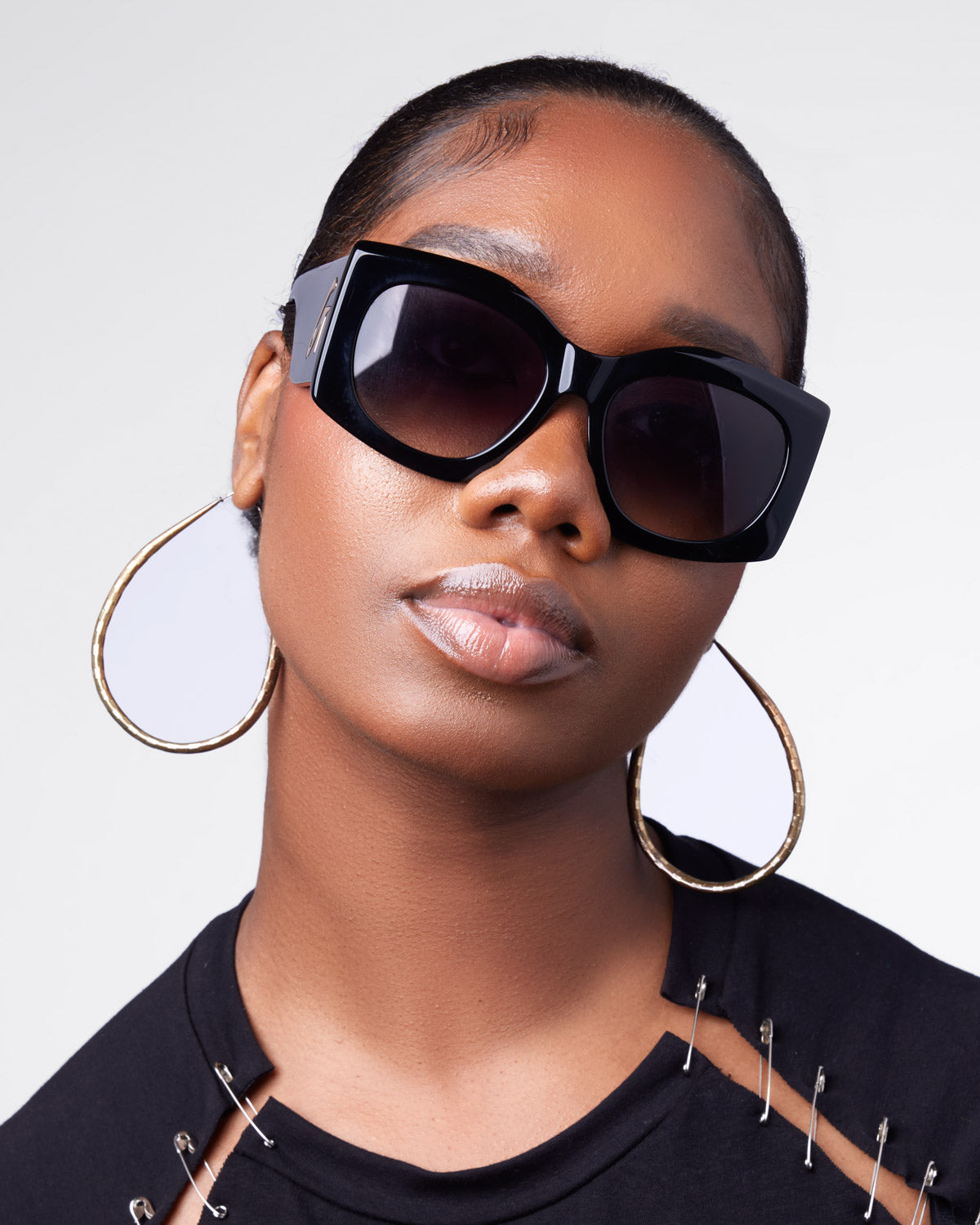 Stylish black oversized sunglasses with a bold frame, worn by a model with hoop earrings and a chic top.
