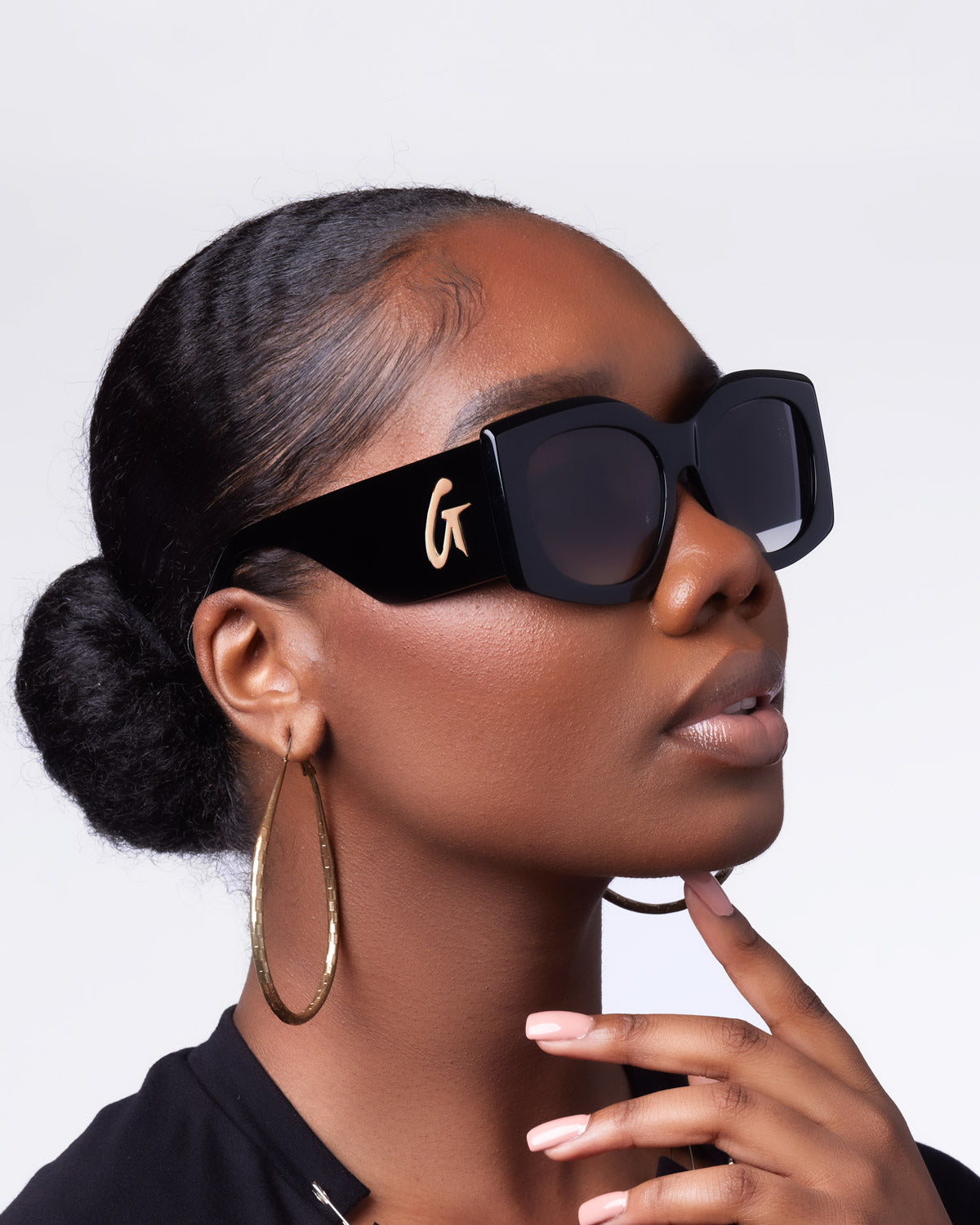Stylish black oversized sunglasses with a gold logo, worn by a model showcasing a chic, elegant look.