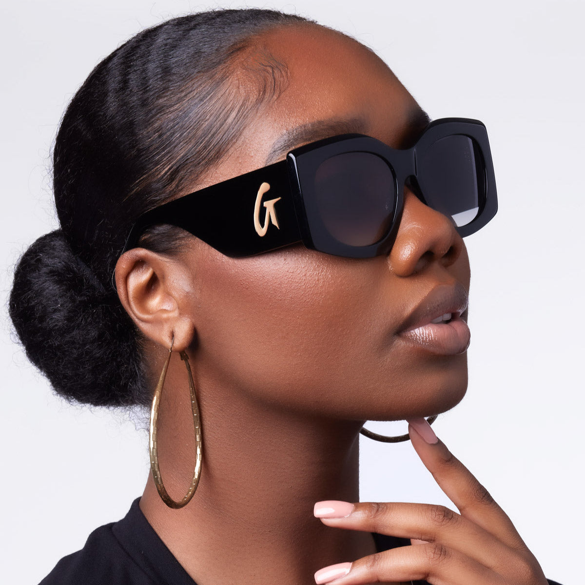 Stylish black oversized sunglasses with a gold logo, worn by a model showcasing a chic, elegant look.