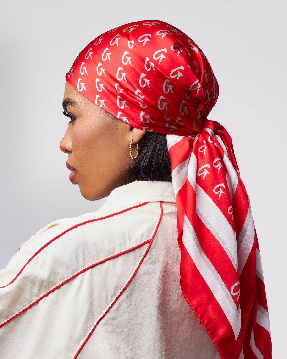 Large red silk scarf featuring a monogram design, styled elegantly around a model's head and neck.