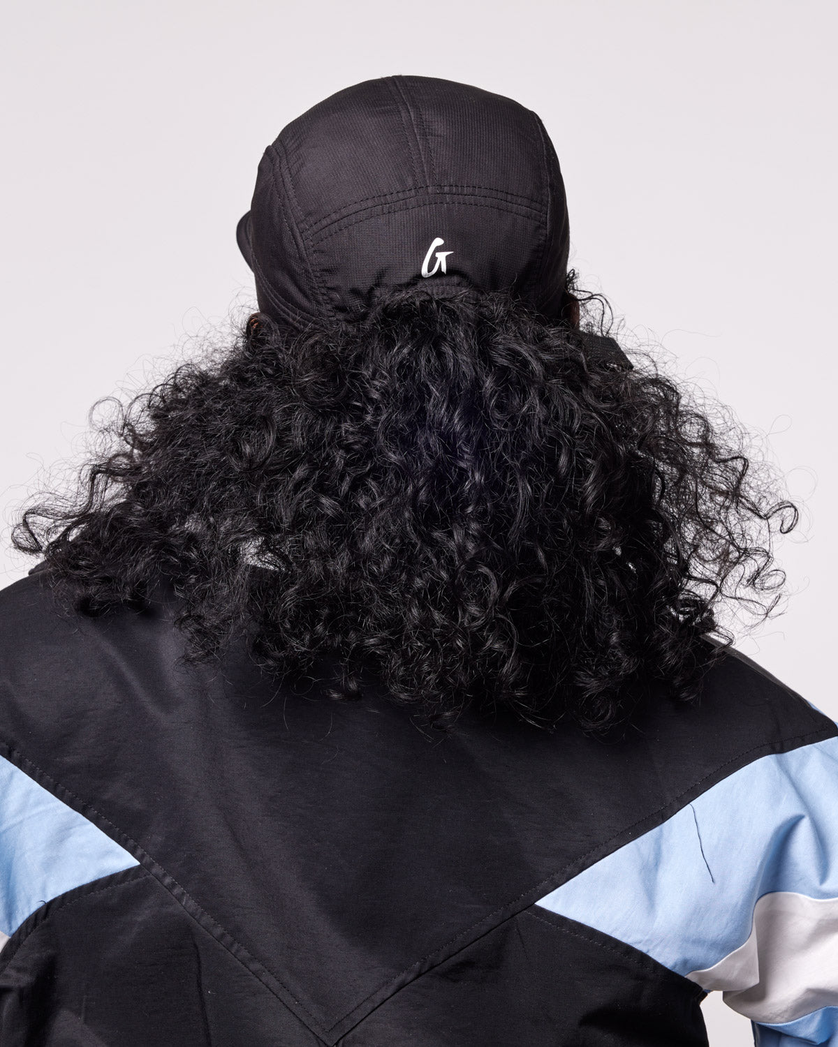 Black athletic 5 panel hat worn by a person with curly hair, showcasing a stylish and sporty look from the back.
