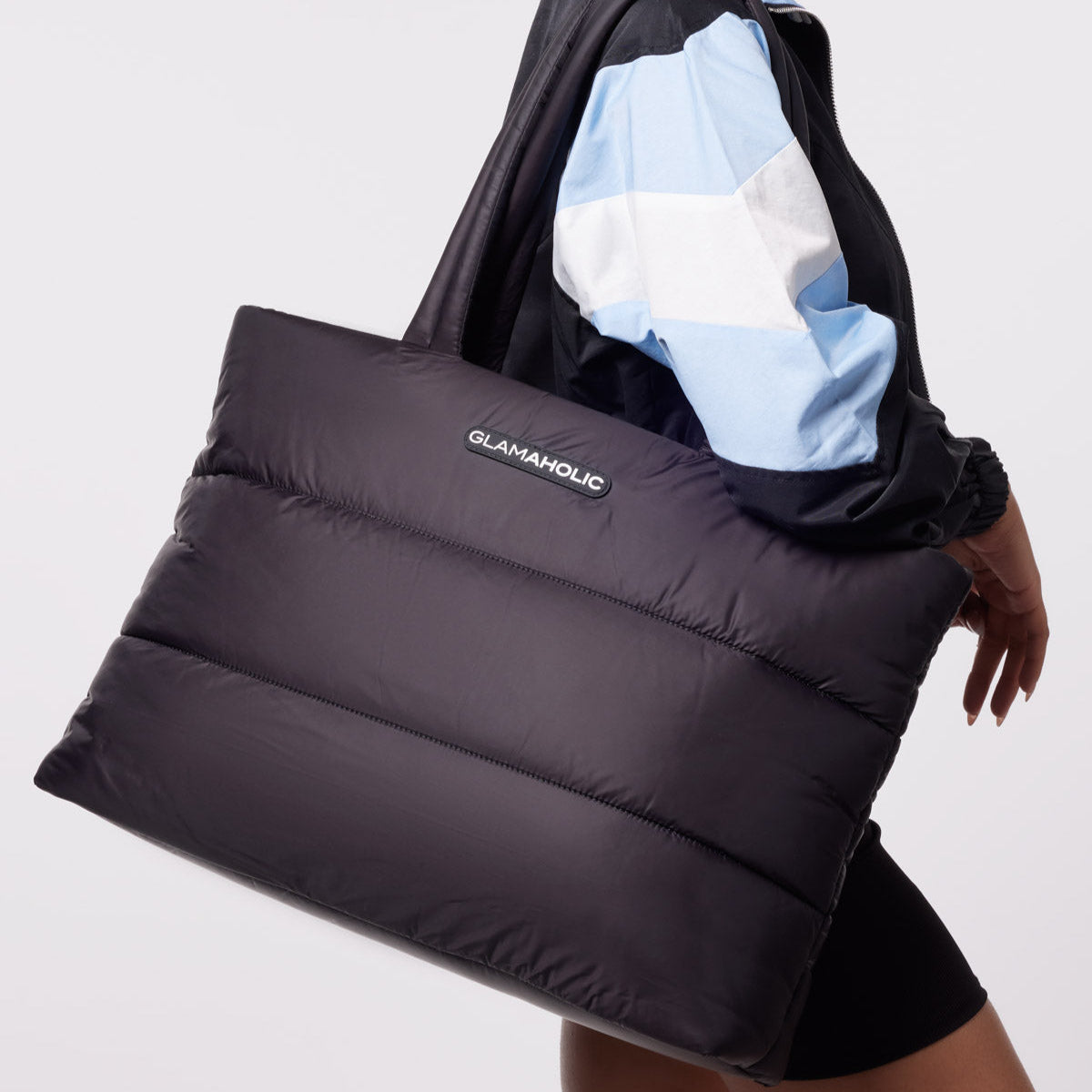 Black athletic nylon tote bag with a puffy design, held by a model wearing a stylish jacket and shorts.