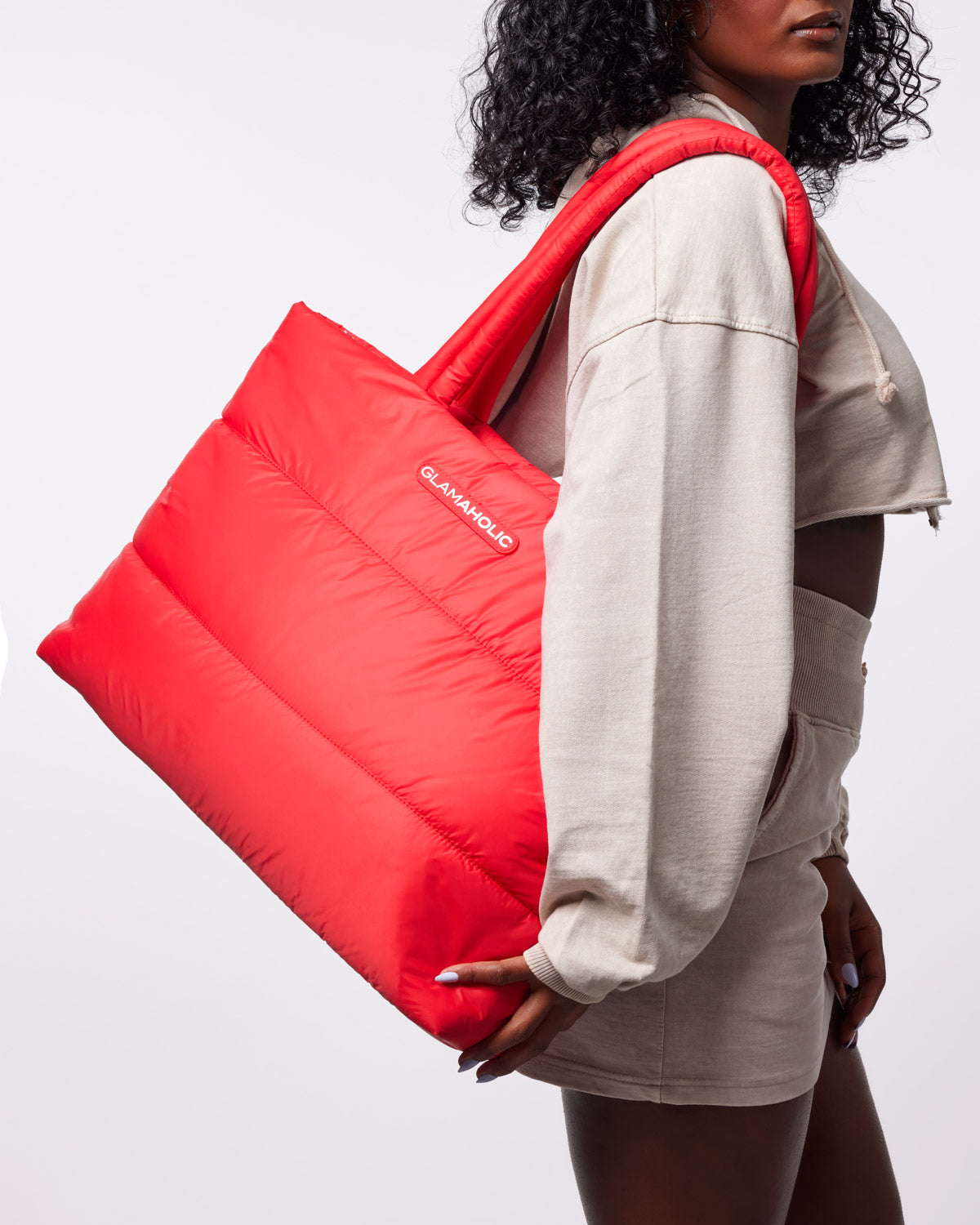 Red athletic nylon tote bag held by a model wearing a cropped beige sweatshirt and matching shorts.