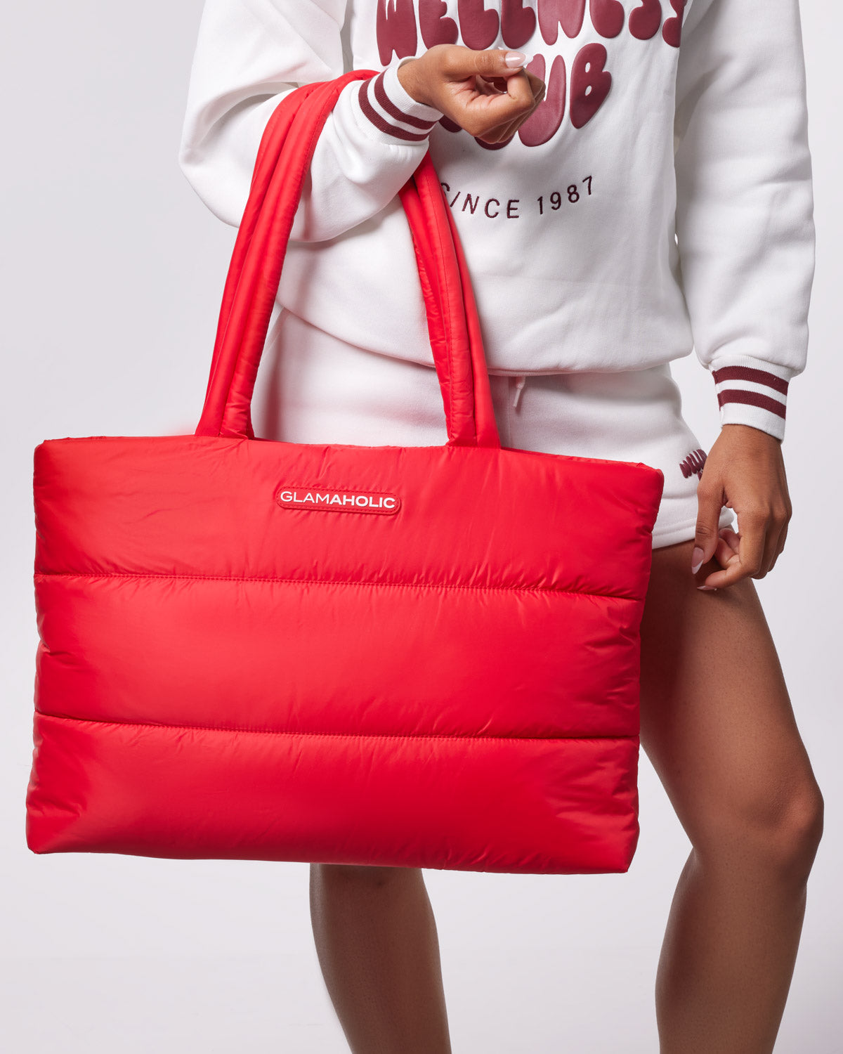 Red athletic nylon tote bag with padded design, held by a person wearing a white sweatshirt and shorts.