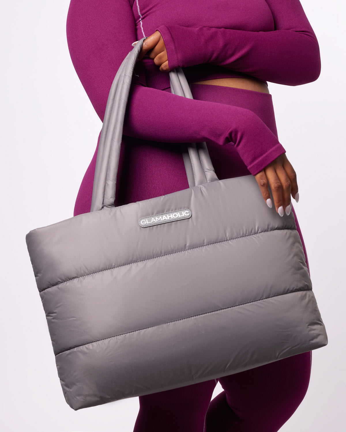 Gray athletic nylon tote bag held by a model in a purple outfit, featuring a padded design and Glam-Aholic logo.