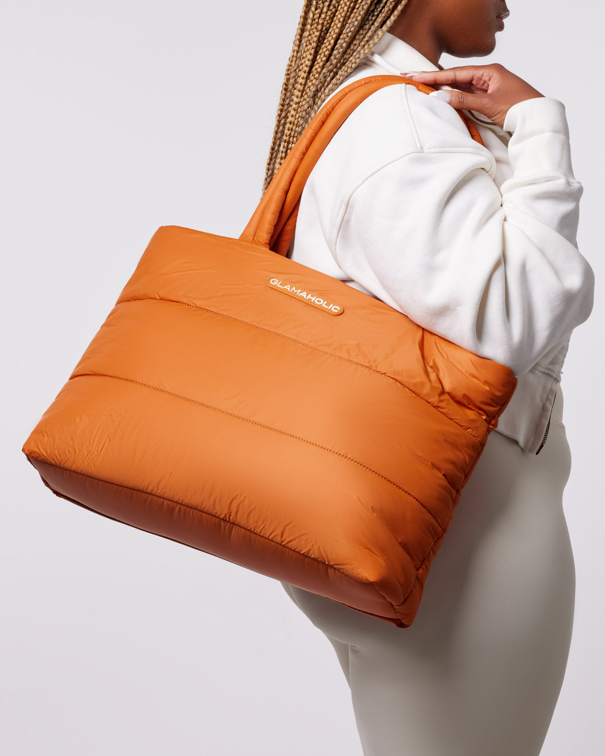 Brown athletic nylon tote bag with a puffy design, held by a person in a white sweatshirt and light-colored pants.