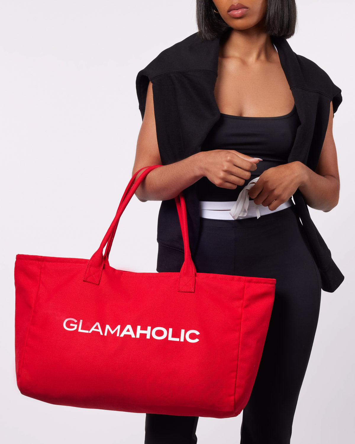 Red athletic canvas tote bag with "GLAMAHOLIC" logo, held by a model in a black outfit. Ideal for stylish storage.