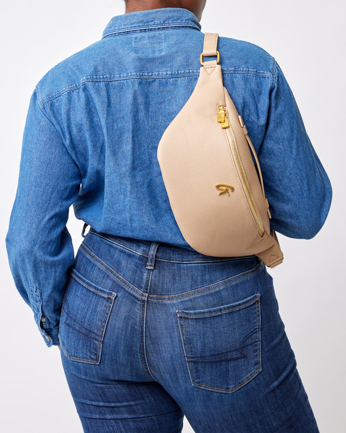 Beige pebble-textured fanny pack worn crossbody on a person dressed in a blue denim jacket and jeans.