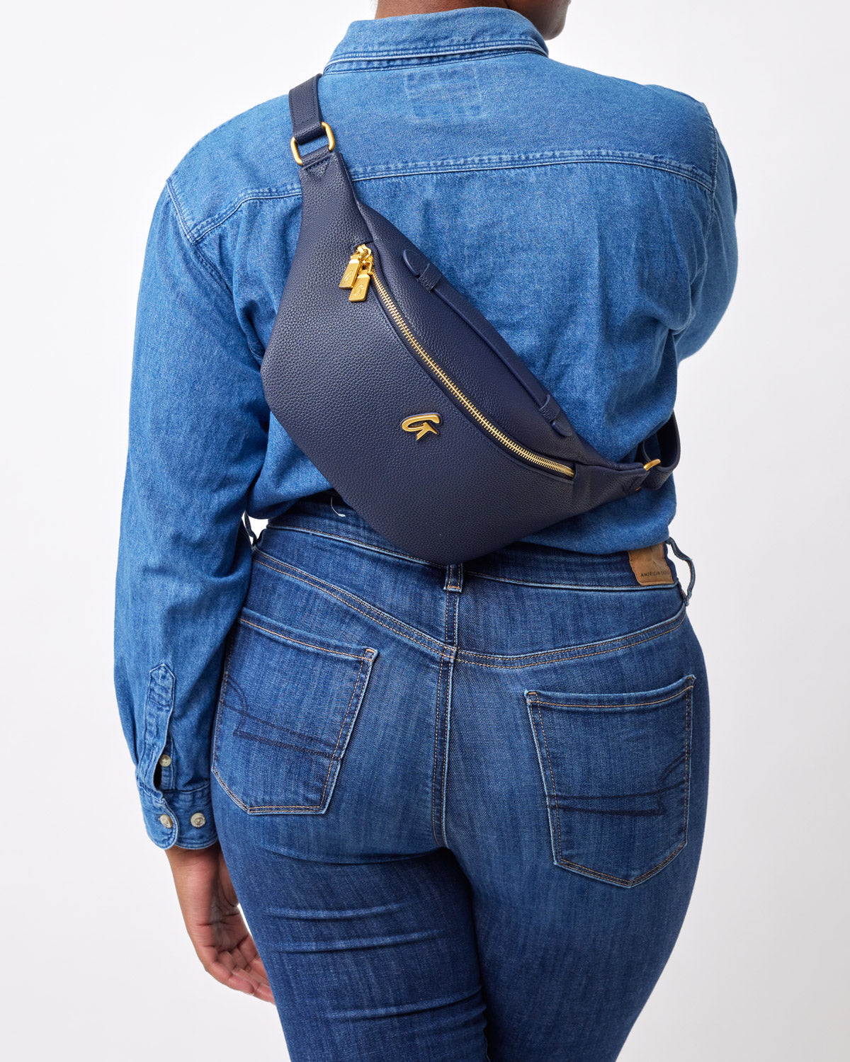 Navy pebble-finish fanny pack worn crossbody on a person dressed in a denim jacket and jeans.