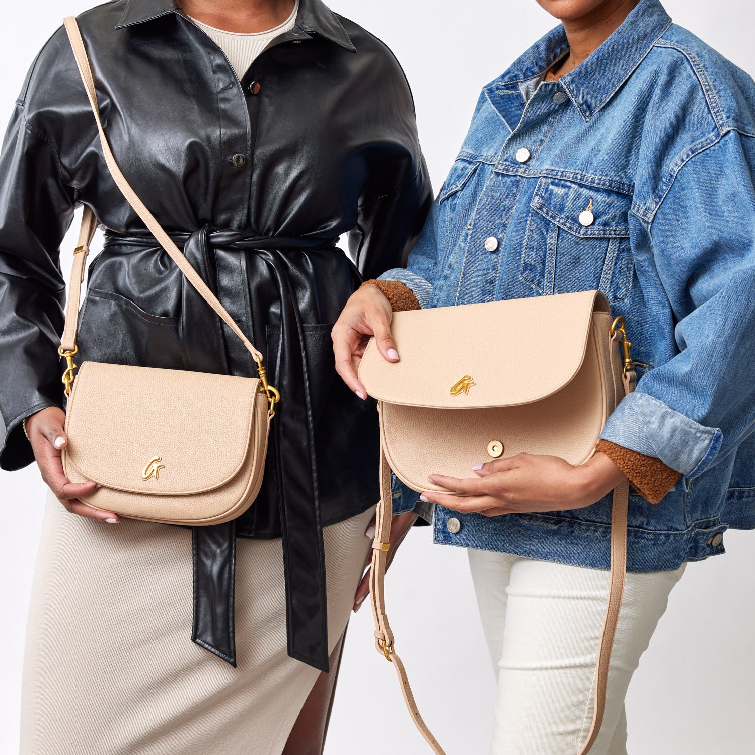Two women hold medium pebble shoulder bags in nude color, featuring gold hardware and adjustable straps.