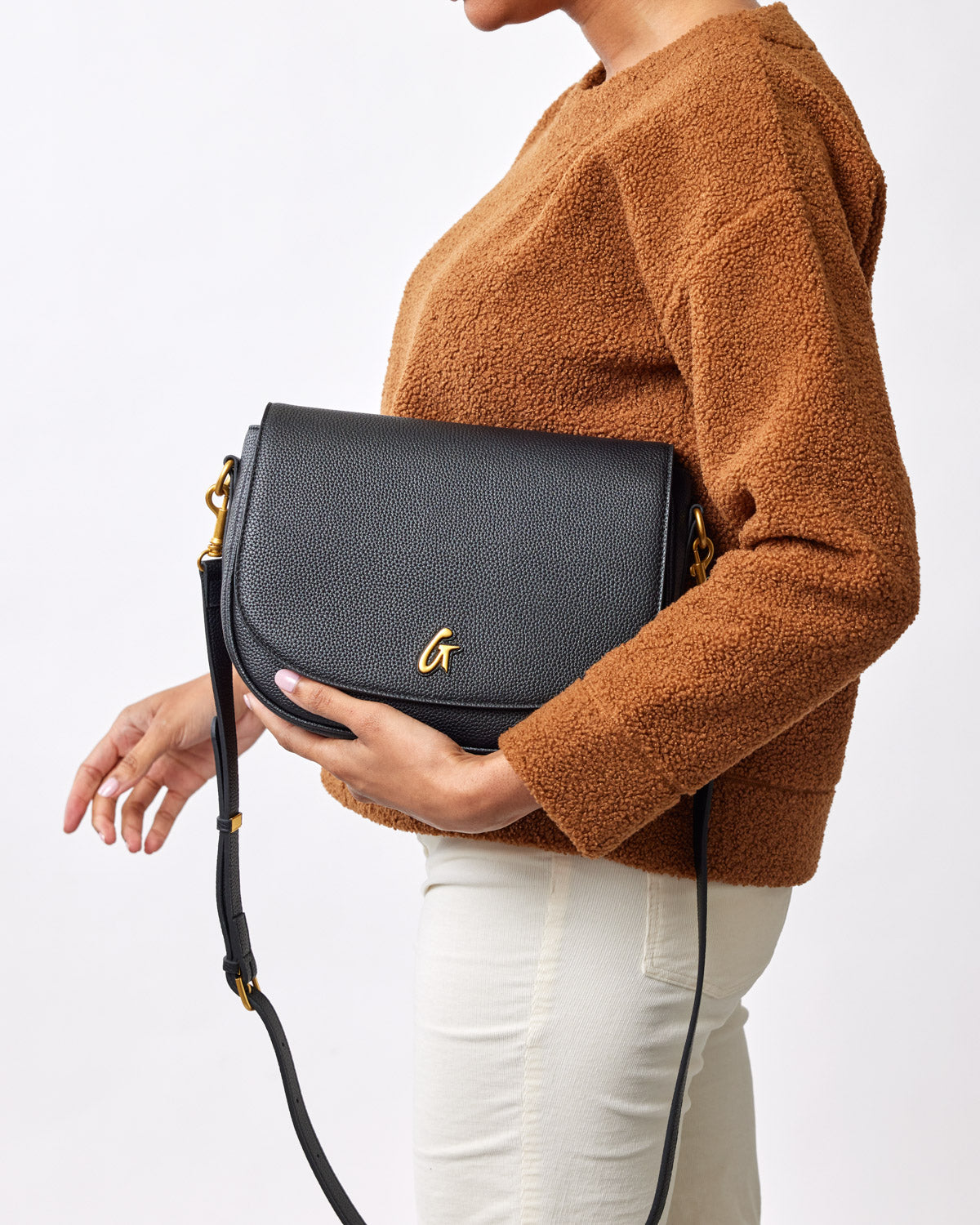 Large black pebble shoulder bag with gold hardware, worn by a person in a brown textured sweater and cream pants.