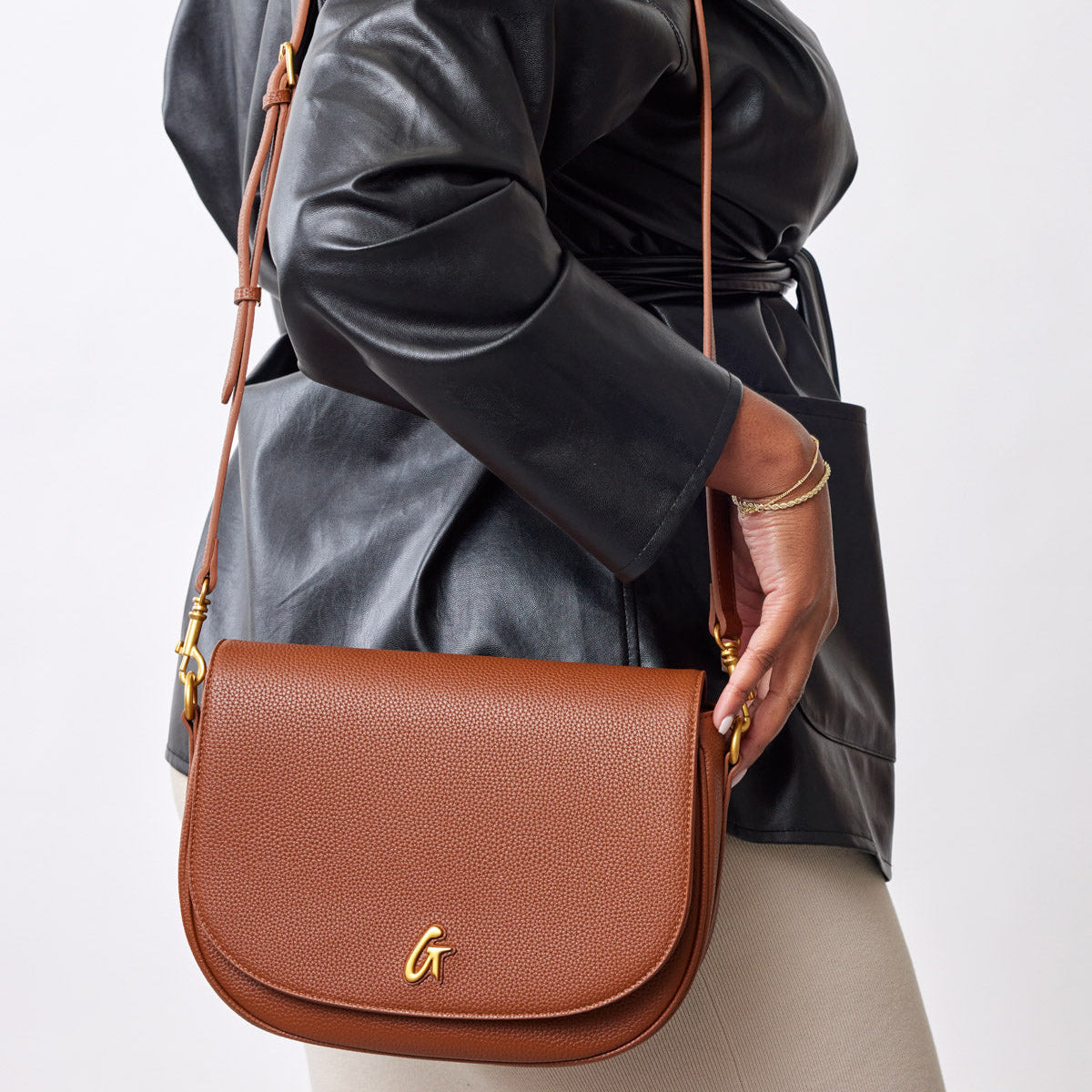 Large brown pebble leather shoulder bag with gold hardware, worn crossbody style by a person in a black leather jacket.