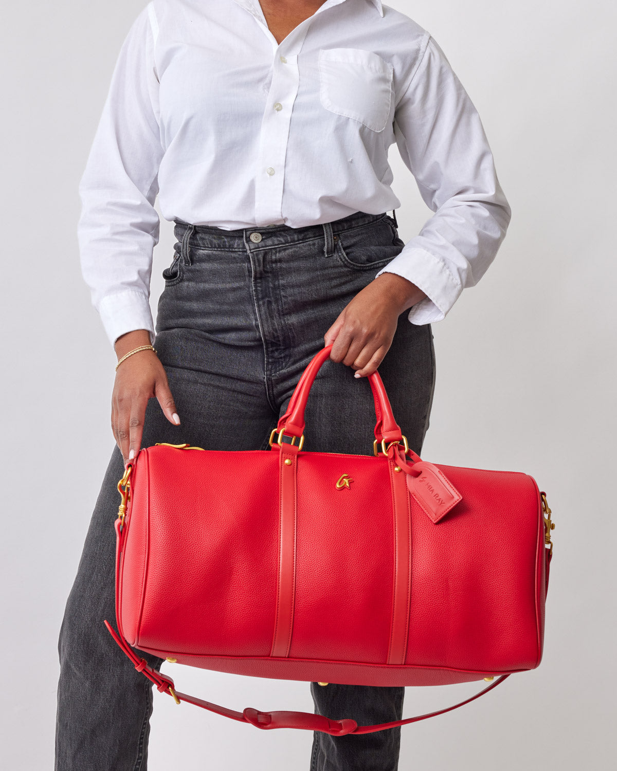 Red Pebble Duffle Bag with gold accents, held by a person wearing a white shirt and black jeans.