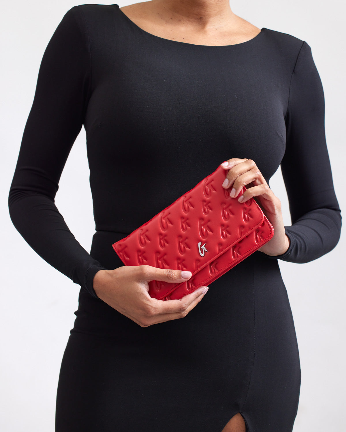 A woman in a black dress holds a red Monogram Silver WOC clutch with embossed G patterns and a silver logo accent.
