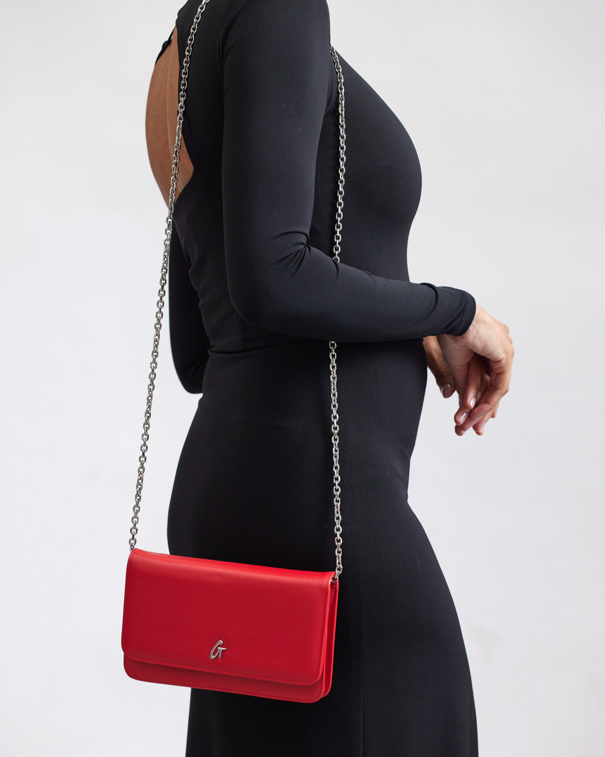 Red leather wallet on chain with silver chain strap, styled with a black fitted dress for a chic look.