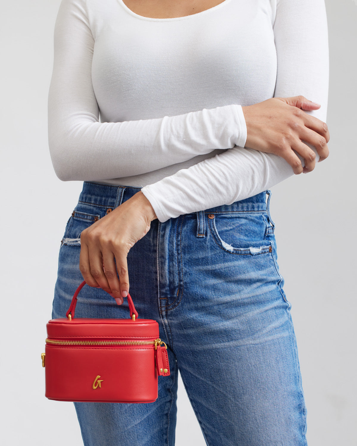 Red mini smooth gold vanity bag held by a woman in a white top and blue jeans, showcasing its stylish design.