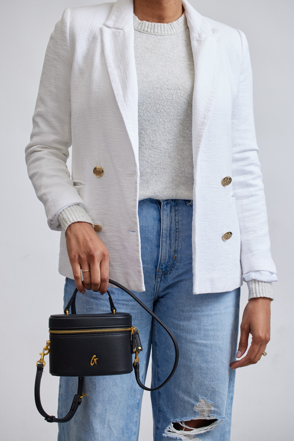Mini Pebble Vanity Bag in black with gold hardware, held by a person wearing a white blazer and distressed jeans.