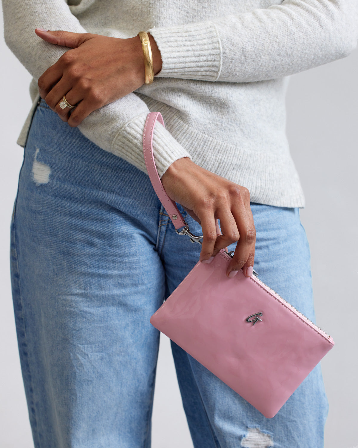 Mini pink mirror wristlet with silver hardware, held by a person wearing a white sweater and blue jeans.