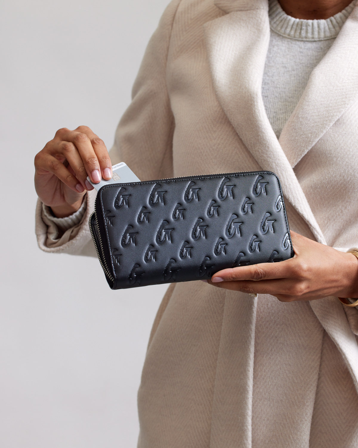 Black matte wallet with embossed monogram G pattern, shown with a person holding a card.