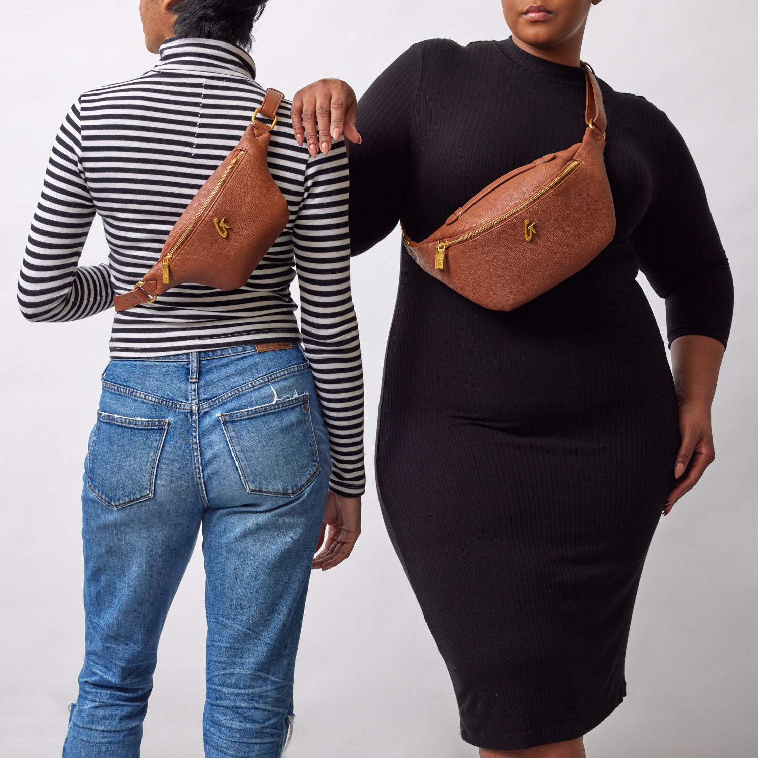 Two women wear matching brown pebble-finish fanny packs across their bodies, styled over casual and fitted black outfits.