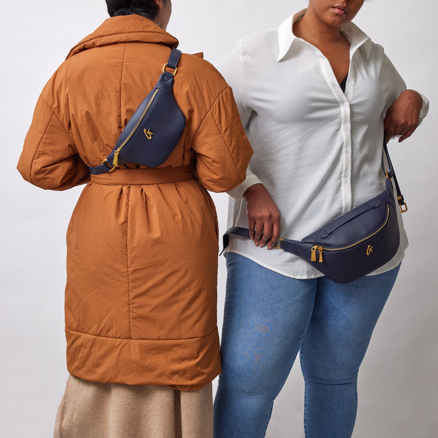Two women wear navy mini pebble fanny packs, one across the chest and the other around the waist, against a plain background.