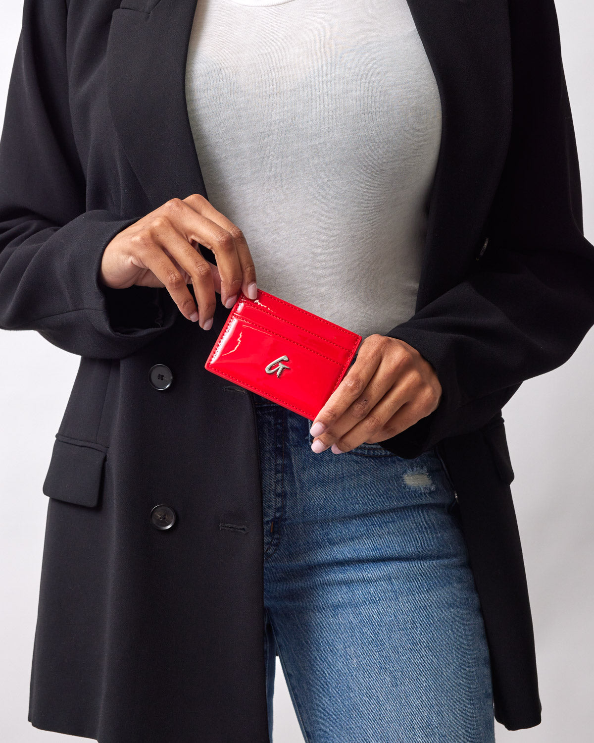 A person holding a red mirror finish silver card holder with a silver logo, dressed in a black blazer and jeans.