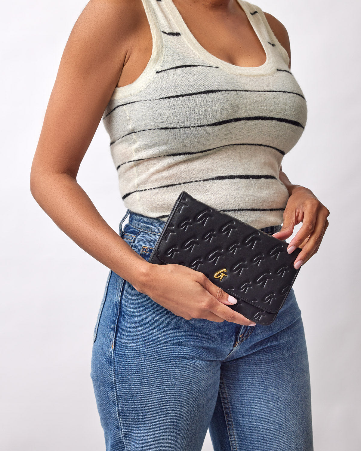 Black Monogram Gold WOC clutch with embossed G pattern, gold logo detail, held by a woman in a striped tank top and jeans.