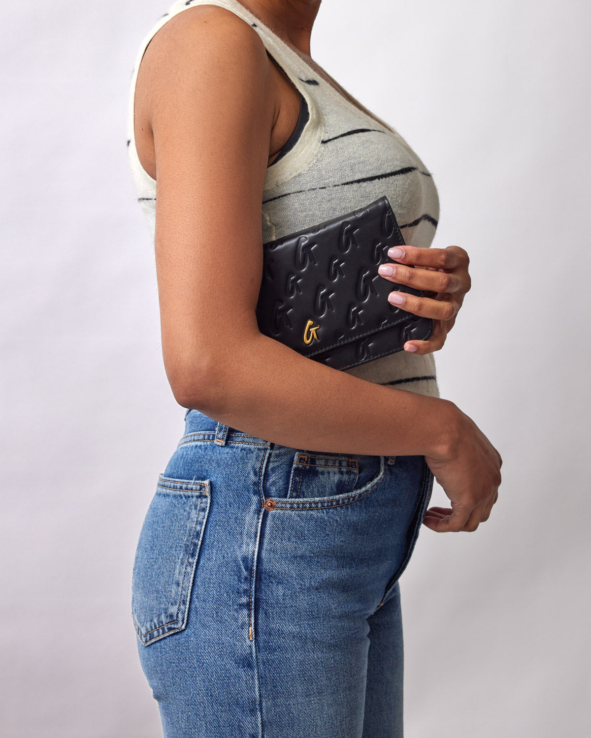 Black Monogram Gold WOC clutch with embossed logo pattern and a small gold logo detail, held against a woman's torso.