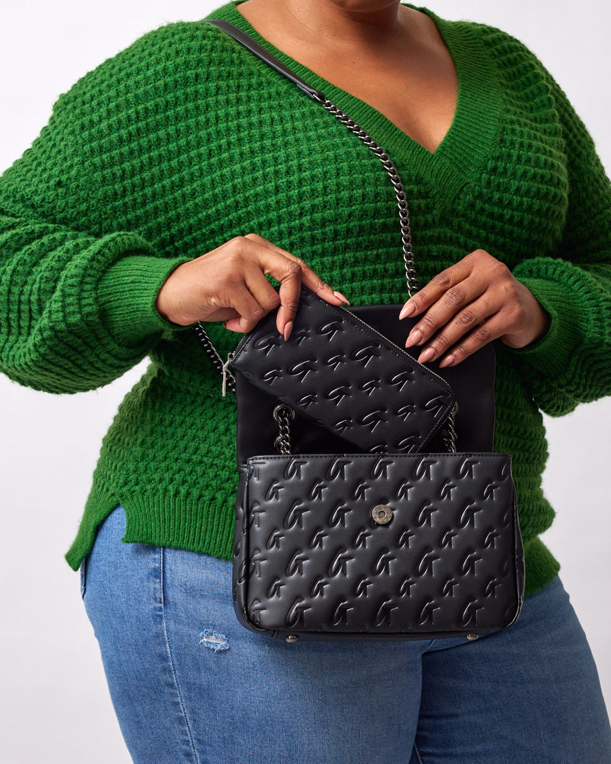 Black medium monogram flap bag with embossed logo pattern, worn with a green sweater and blue jeans.