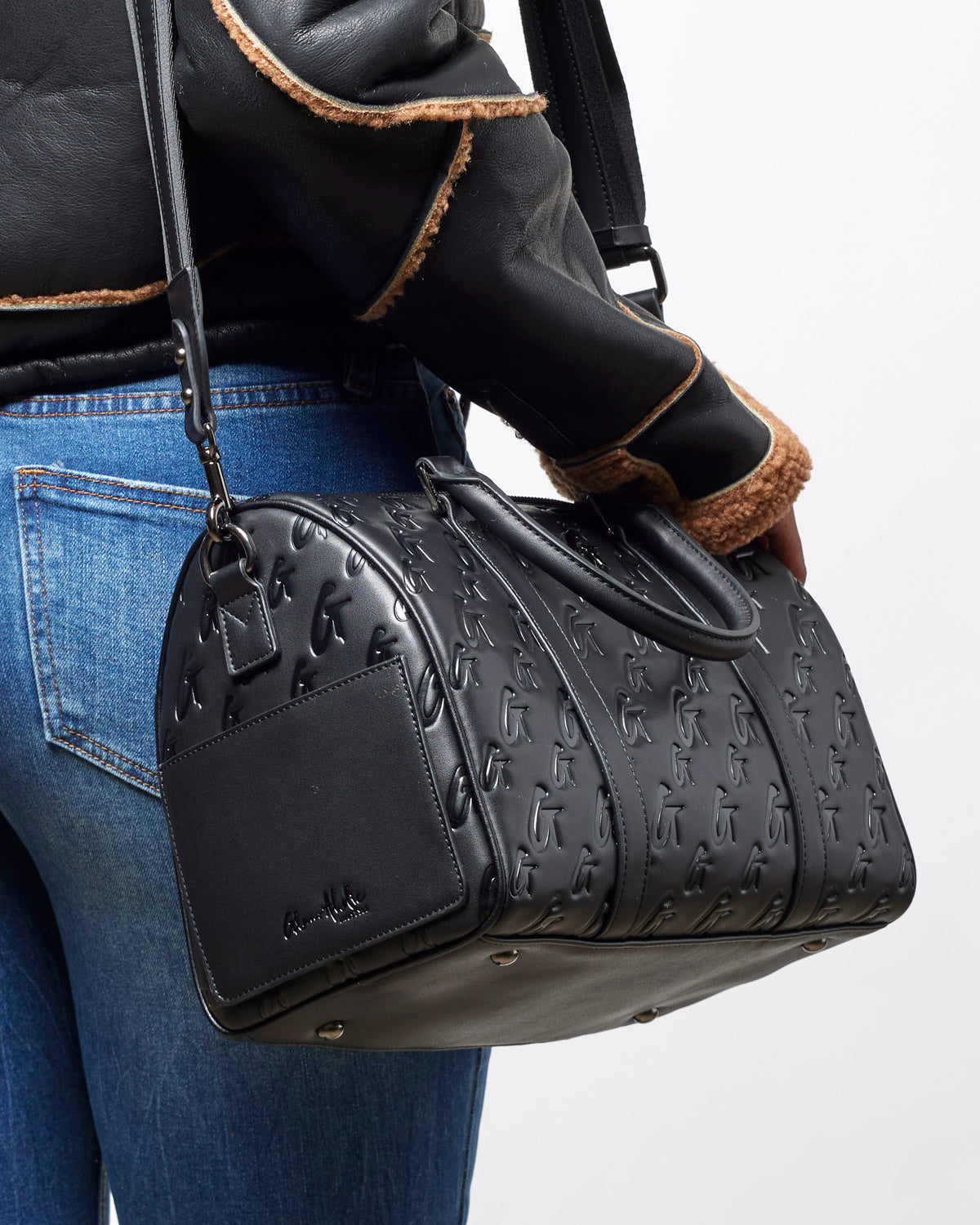 Large black monogram gal Boston bag with embossed logo, carried by a woman in a stylish outfit.