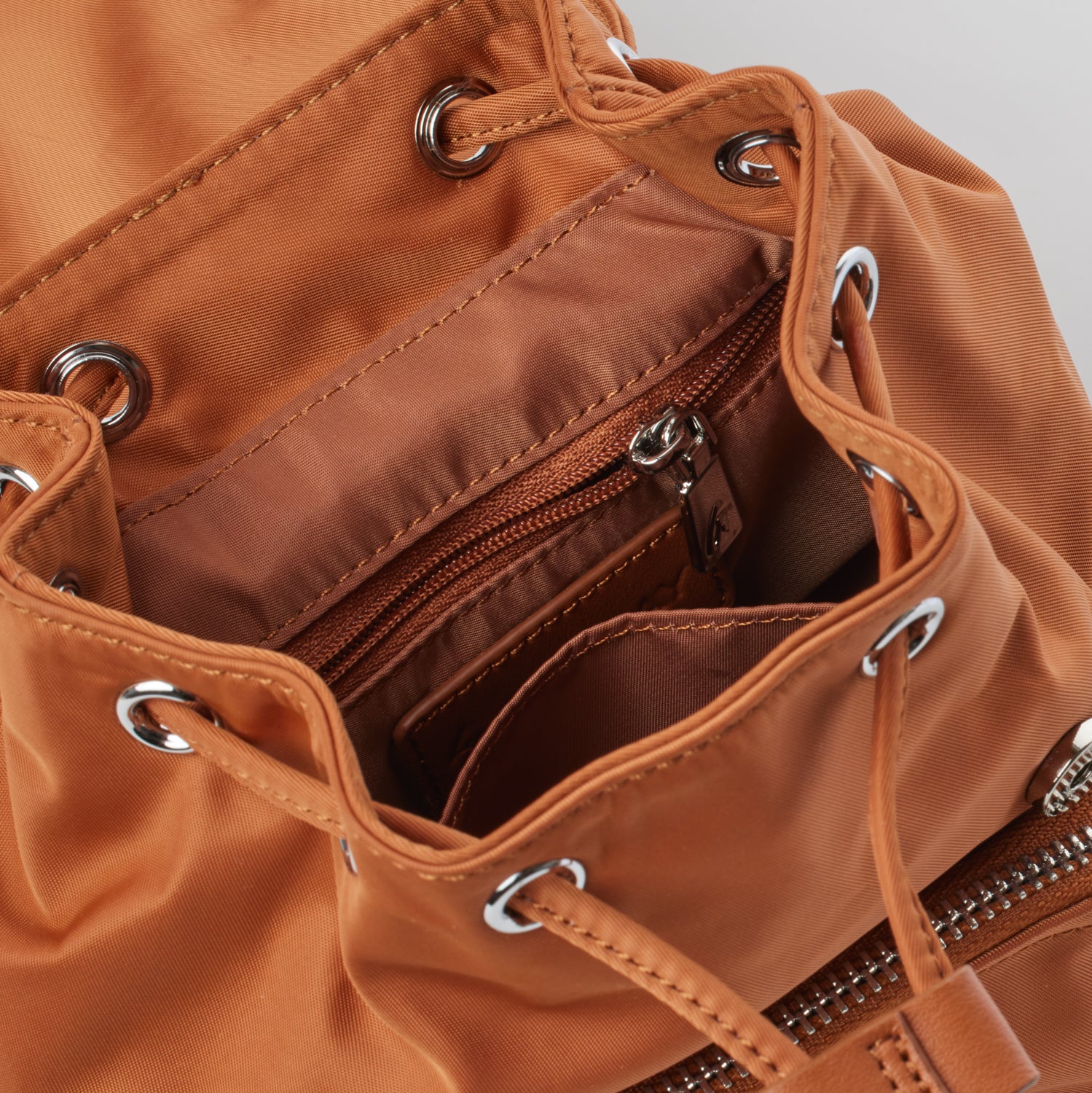 Mini brown nylon backpack with interior zip pocket, drawstring closure, and metal eyelet accents.