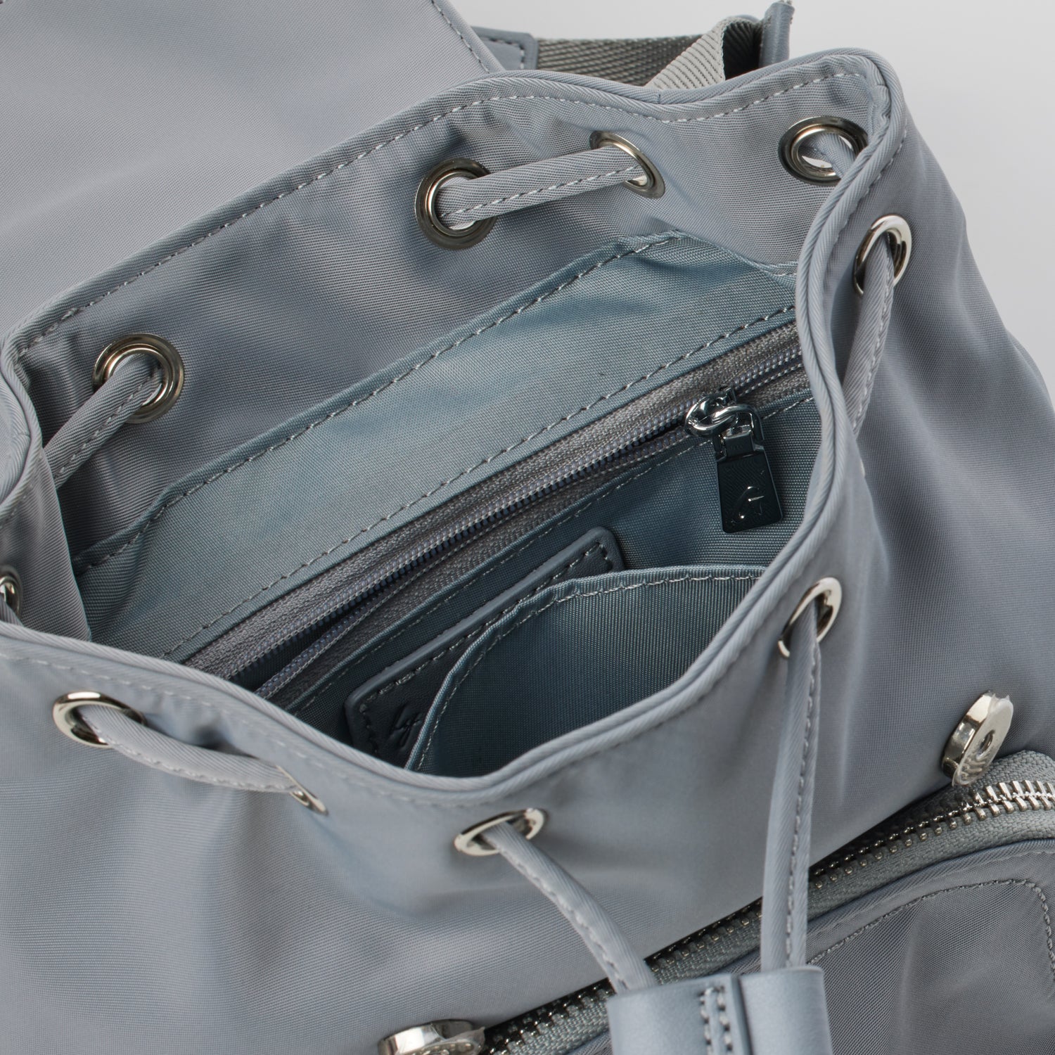 Close-up of a gray mini nylon backpack with metal eyelets, drawstrings, and a zippered interior pocket.