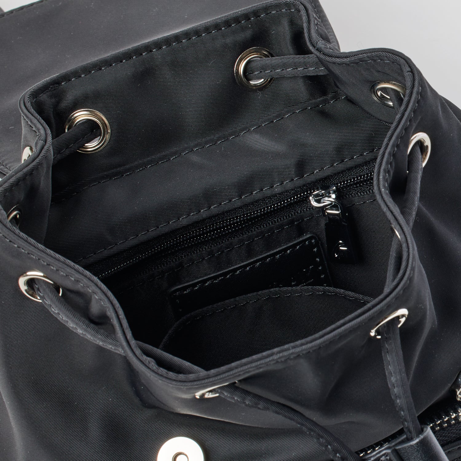Close-up of a black mini nylon backpack showing interior compartments, zipper pocket, and metal eyelets for drawstrings.