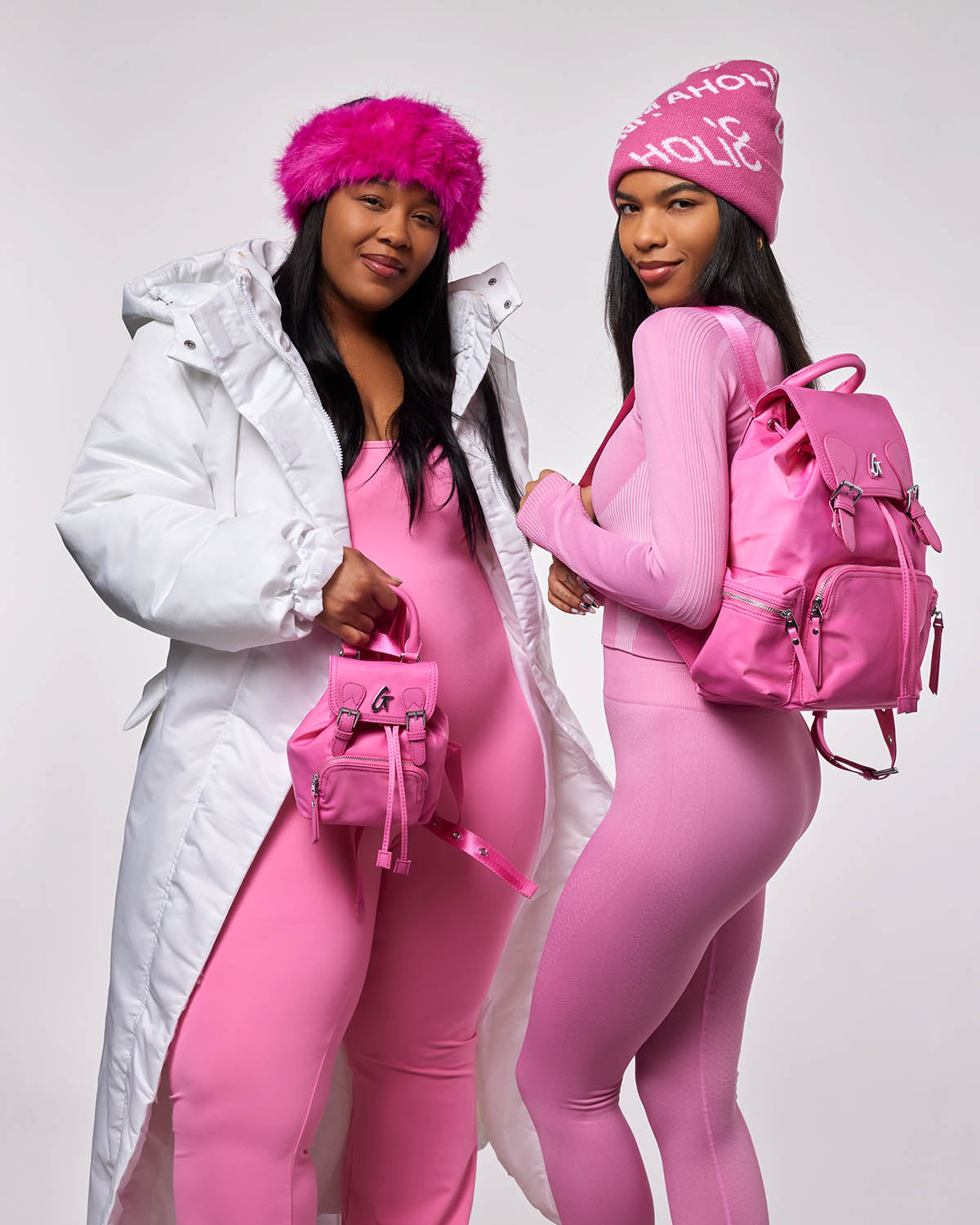 Two women in stylish pink outfits showcase a hot pink nylon backpack, highlighting its trendy design and functionality.