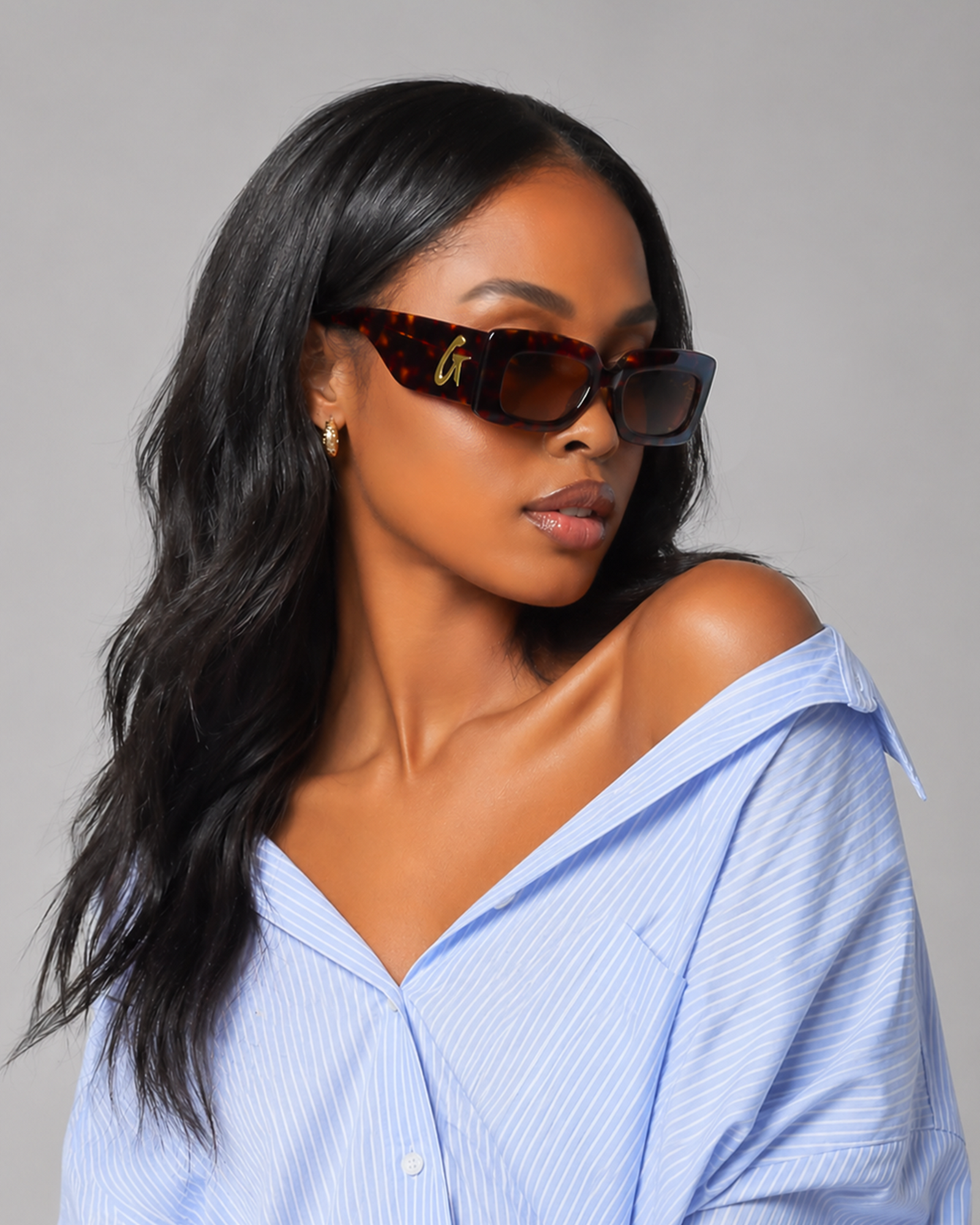Stylish model wearing tortoise sunglasses with a chic blue striped shirt, showcasing affordable luxury eyewear.
