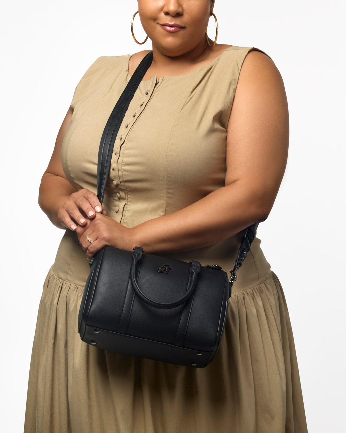 Medium black Boston bag held by a woman in a beige dress, showcasing a stylish and versatile accessory for everyday use.