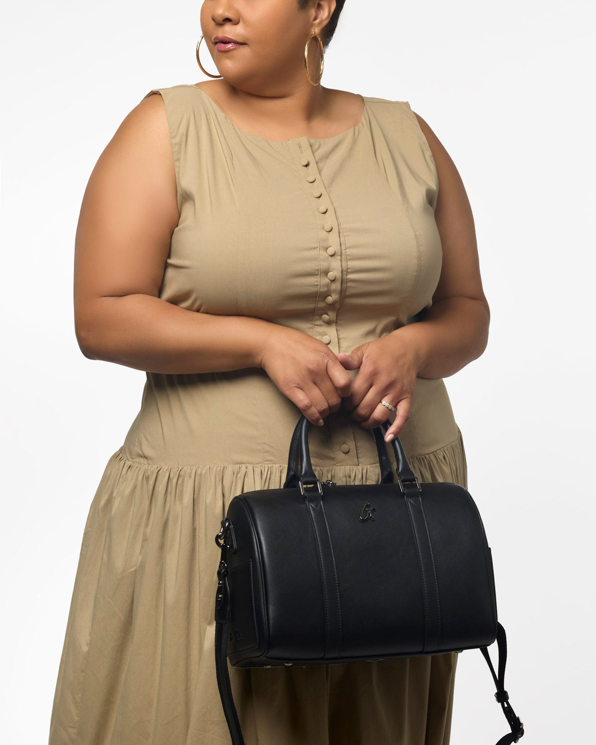 Large black Boston bag held by a woman in a beige dress, showcasing its stylish design and versatile use.