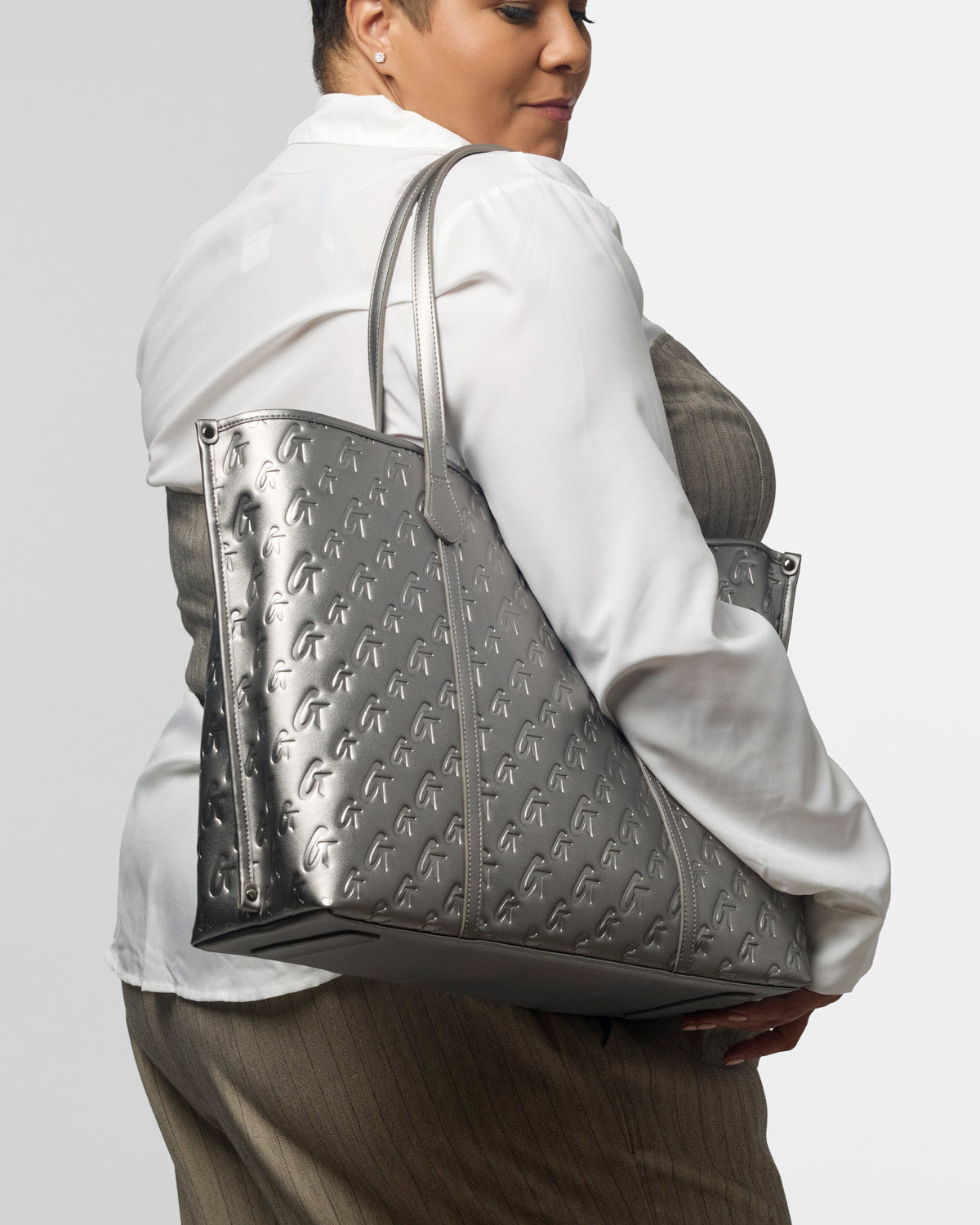 XL Monogram Sleek Tote in platinum, featuring a stylish embossed design, carried by a woman in a white blouse.