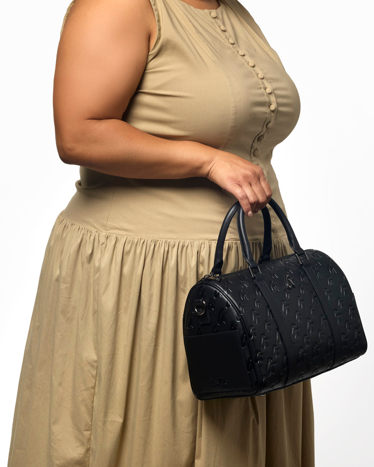 Large black monogram gal Boston bag held by a woman in a beige dress, showcasing its stylish design and luxury appeal.